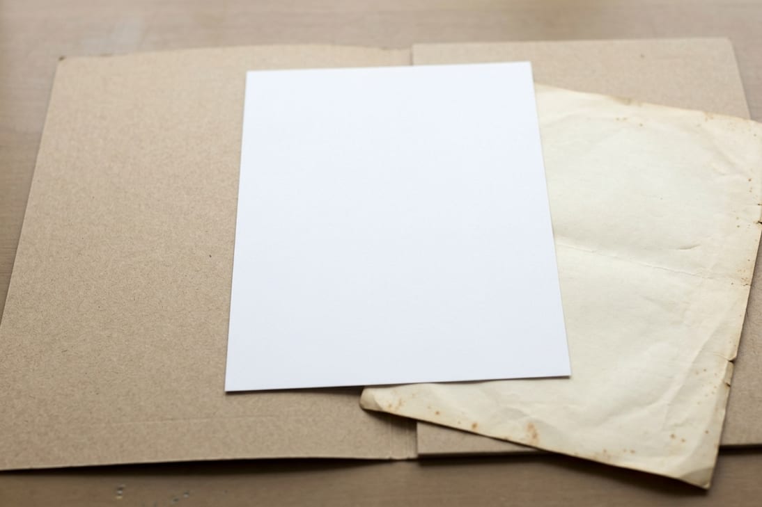 A crisp blank sheet resting over an older yellowed sheet in an archive folder